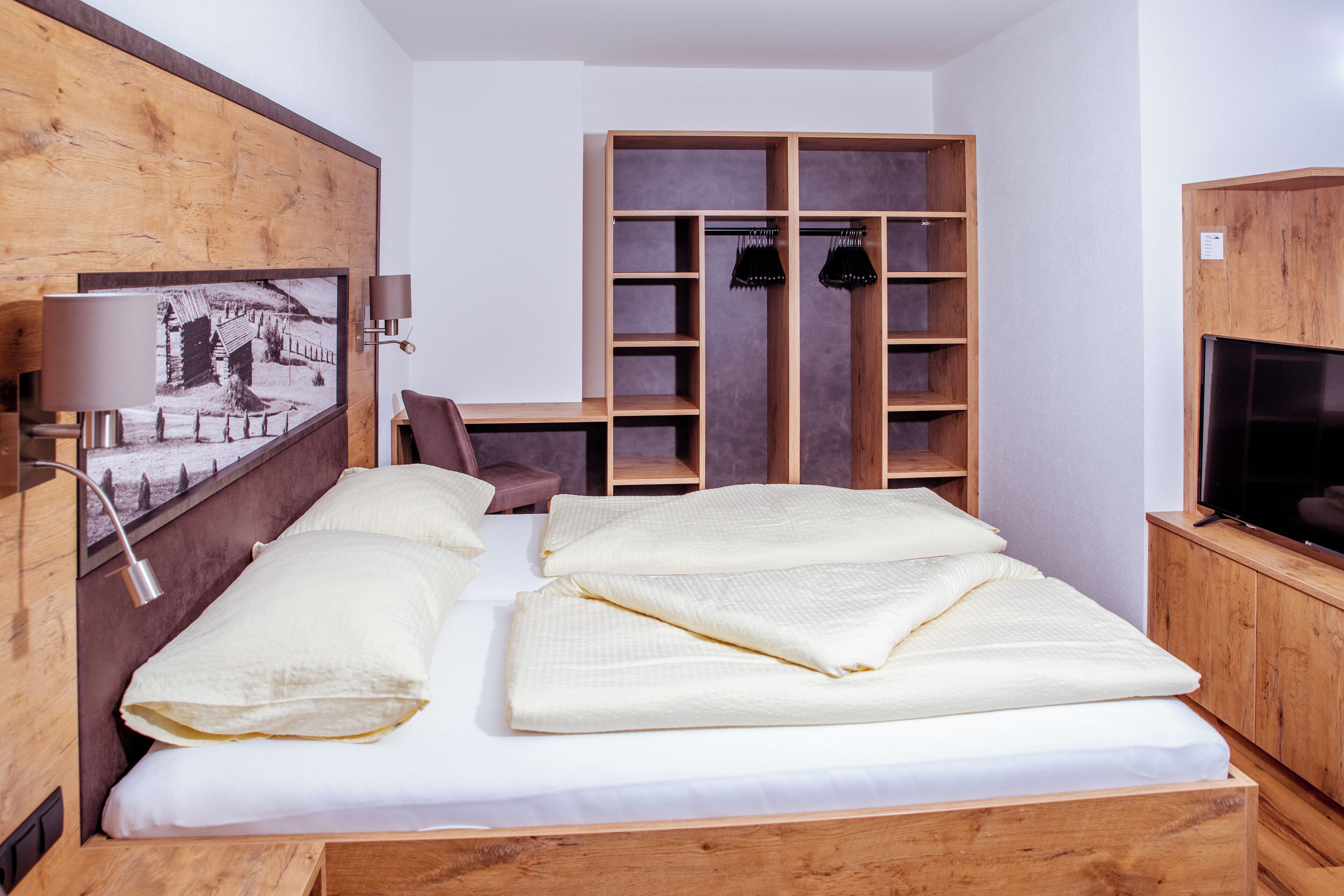 A bedroom with a wooden bed, a desk, a wardrobe, and a television.