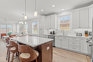 A modern kitchen with white cabinets, a central island with bar stools, and a dining area with a table and chairs. - Steps to Beach: Ocean Views, 5 Decks, 3 Cars, Loaded with Amenities! (Seaside Heights)