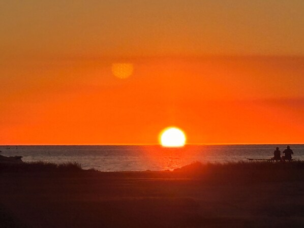 Un atardecer sobre el océano con siluetas de personas en la orilla.