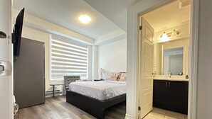 A bedroom with a bed, bedside table, lamp, and a window with blinds. - Your Private Space - Nothing Shared (Brampton)