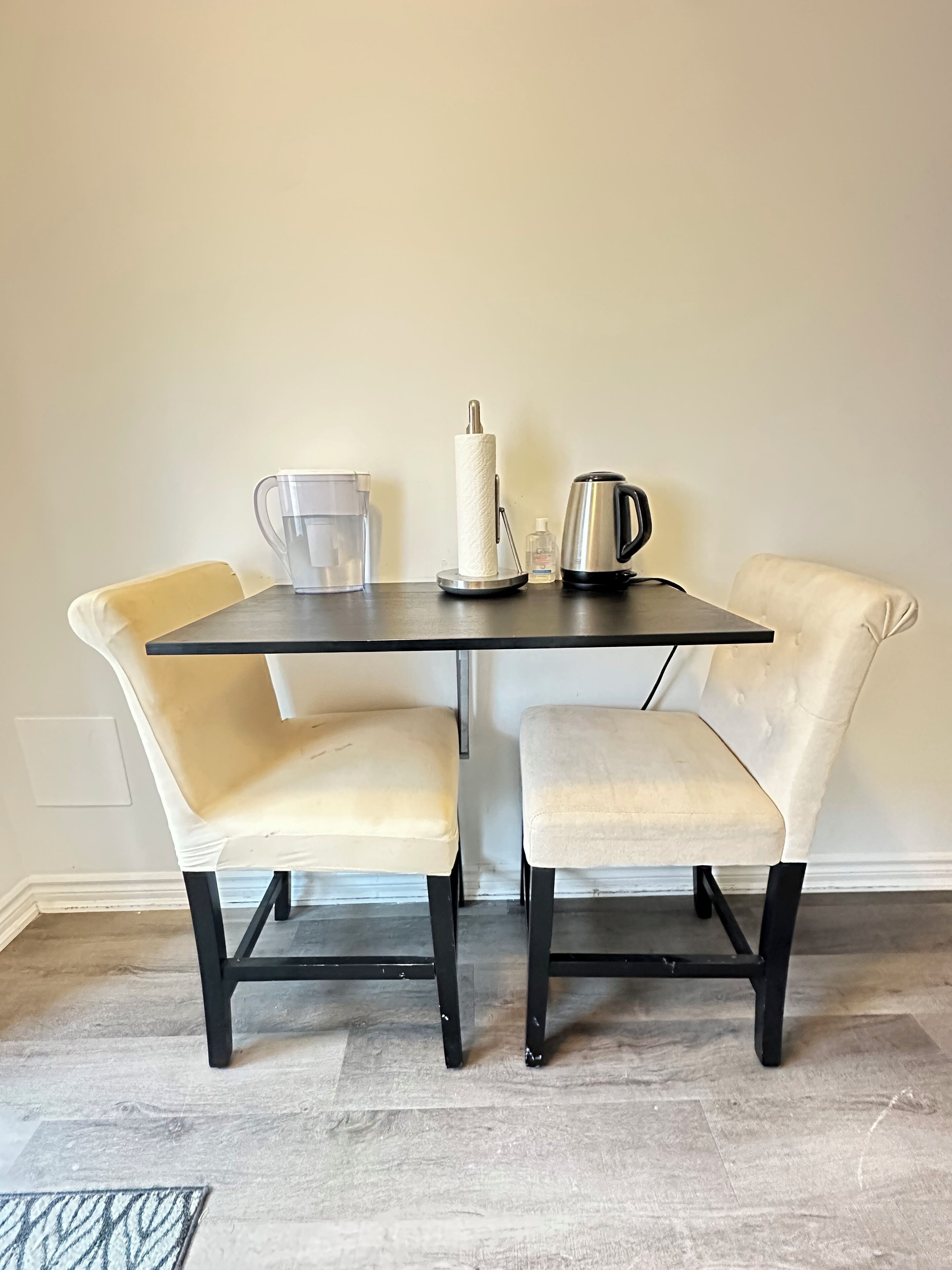 A dining table with two chairs, a paper towel holder, a glass pitcher, and a kettle.