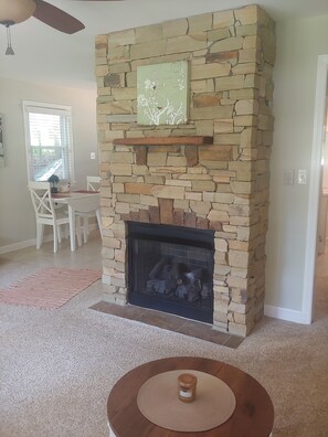 A stone fireplace with a mantel, a dining area with chairs and a table, and a ceiling fan. - Cozy Cork Cottage Asheville South / Private/Secure/Quaint/ Near Airport (Arden)