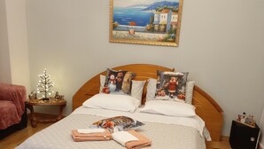 A neatly made bed with a patterned bedspread, pillows with holiday-themed designs, and a small table with a decorative item beside it.