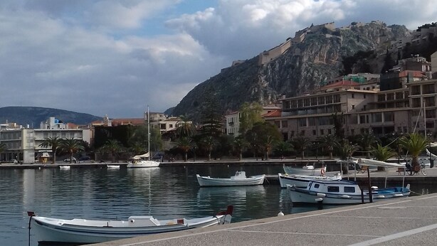 A marina with boats docked, a pebble beach, and buildings in the background.