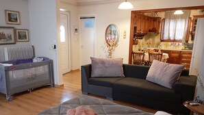 A living room with a grey sofa, a baby changing station, and a dining area visible through an open door.