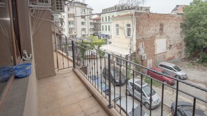 Un balcón con barandilla metálica que da a una calle con coches estacionados y edificios.