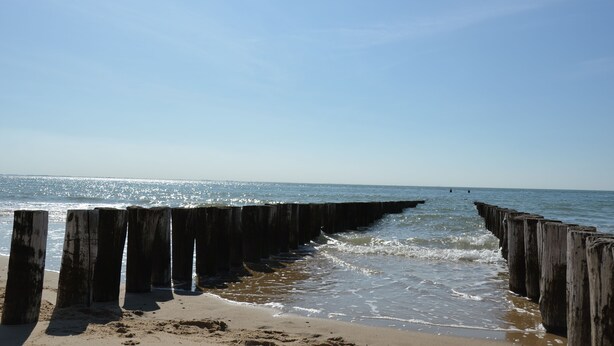 A wooden pier extending into calm ocean waters with clear skies. - Luxuriöses Chalet in Fußnähe zum Strand (Biggekerke)