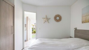 A bedroom with a large bed, a wooden wardrobe, a starfish decoration, and a sunburst wall art piece. - Luxuriöses Chalet in Fußnähe zum Strand (Biggekerke)