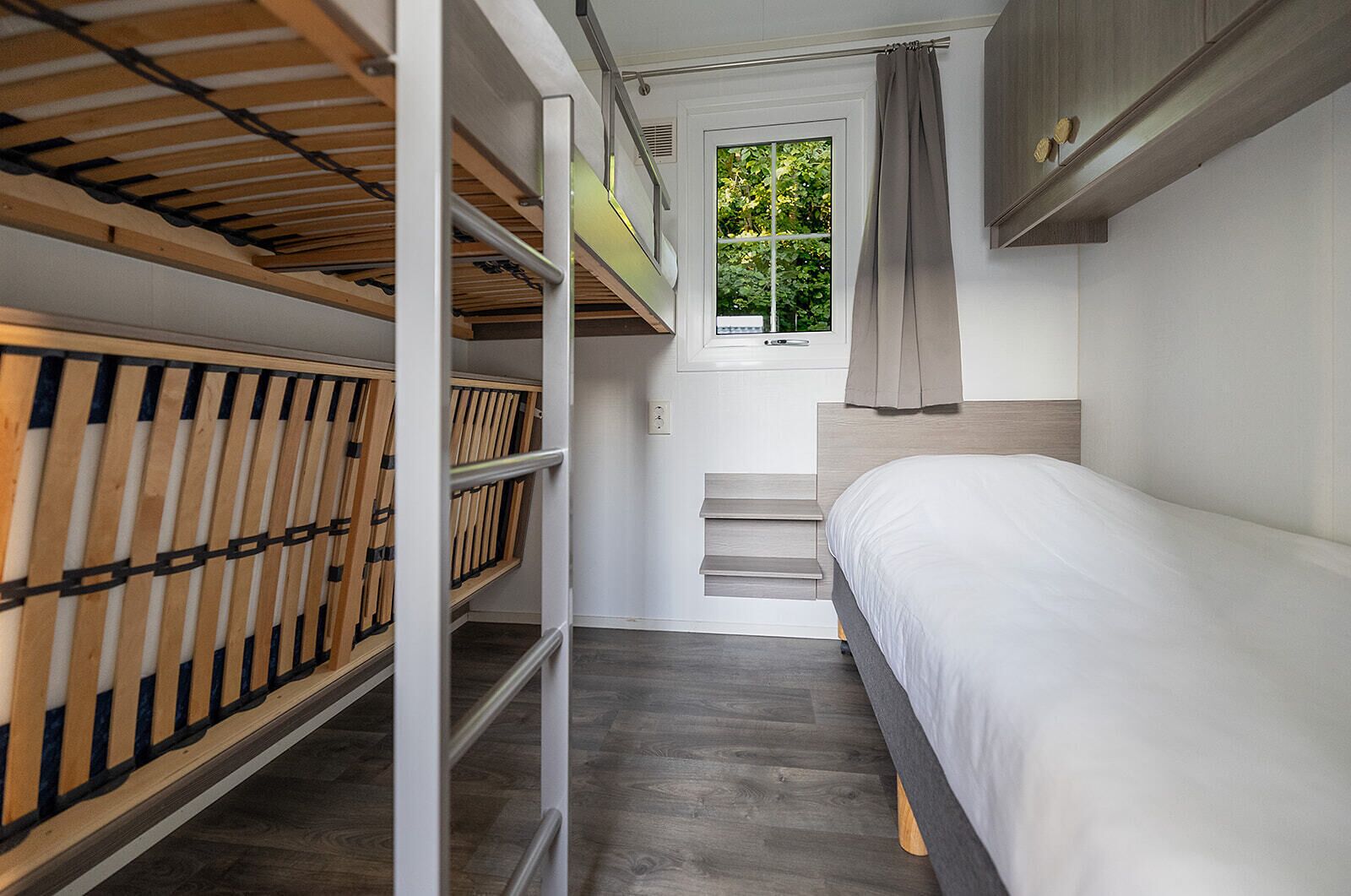 Un dormitorio compacto con una cama litera, una cama individual, una ventana con cortinas y una escalera.