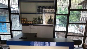 A bar area with a counter, shelves with bottles, and a view through large windows. - Hotel D4 Red Mud (Thuli Bheri)