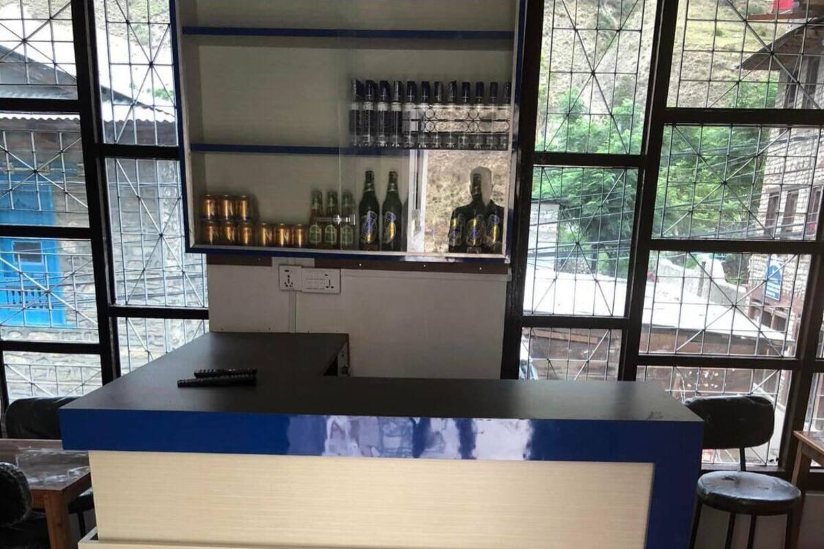 A bar area with a counter, shelves with bottles, and a view through large windows.