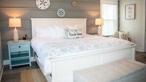 A bedroom with a large bed, two bedside tables with lamps, a bench, and decorative wall clocks. - Luxury 6-Bedroom Home with Private Pool, Elevator & Family-Friendly Comfort (Hilton Head)