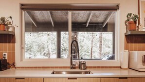 Una cocina con armarios de madera, un lavamanos de acero inoxidable y una ventana con vistas a árboles.