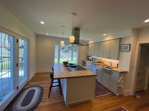 A modern kitchen with a central island, wooden flooring, and large windows.