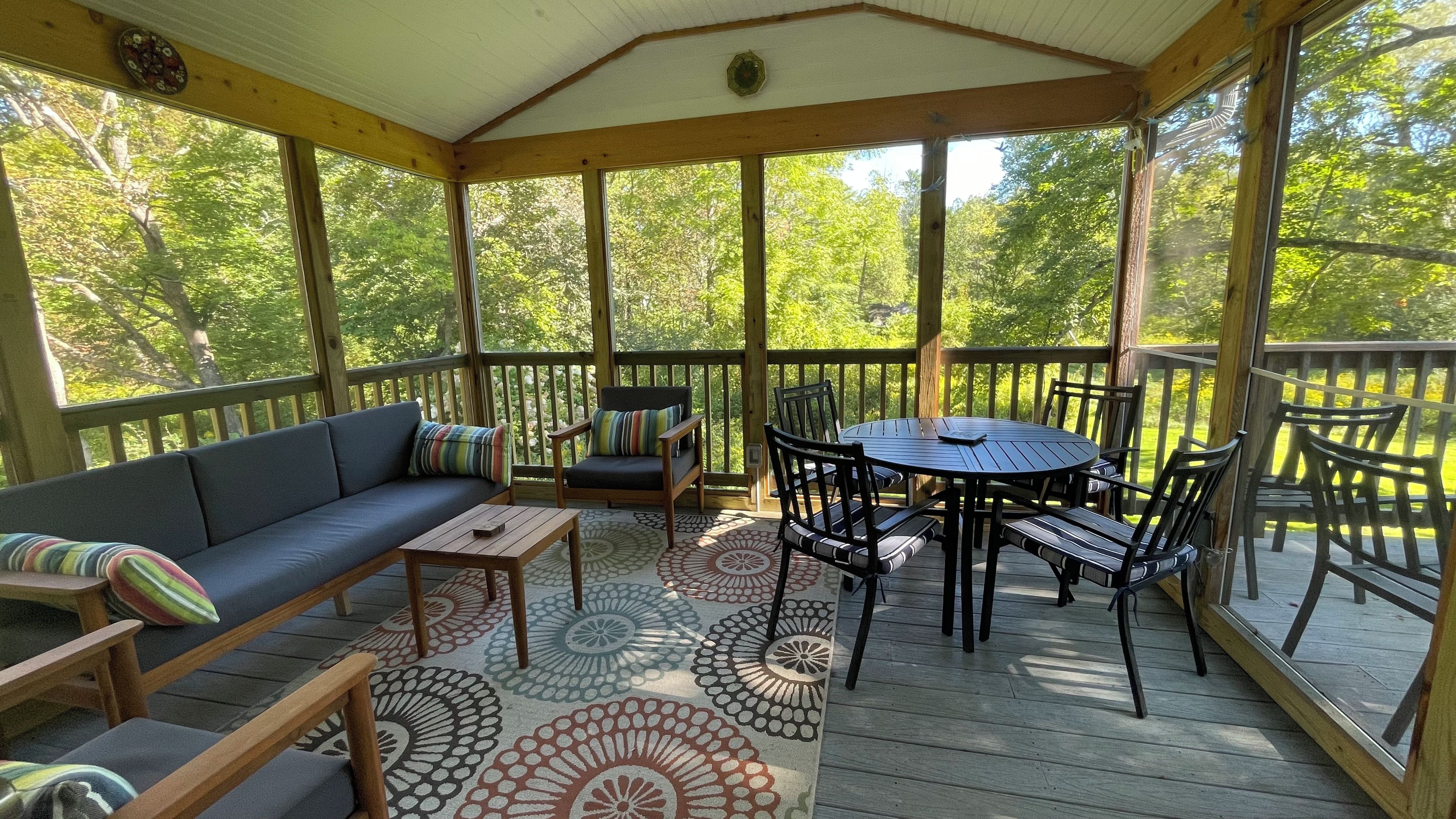 Une terrasse extérieure couverte, aménagée avec un canapé, des chaises, une table et un revêtement de sol à motifs.