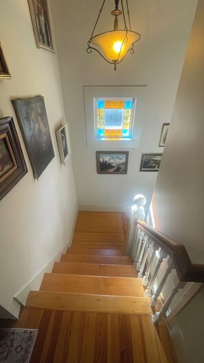 A wooden staircase with a handrail, a hanging light fixture, and framed artwork on the walls.