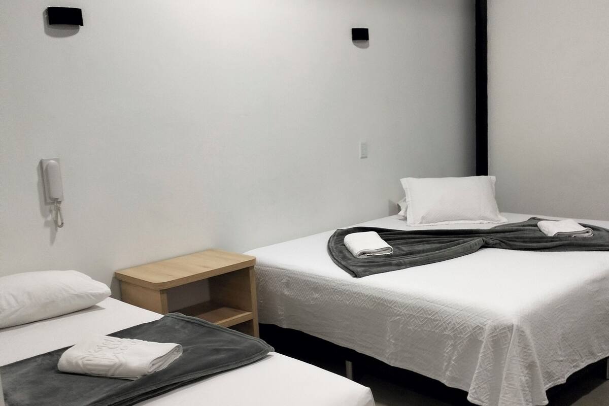 A hotel room with two single beds, a wooden nightstand, a small shelf, and a telephone.