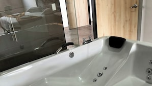 Un baño moderno con una bañera blanca grande, una ducha con cerramiento de vidrio y una puerta de madera.