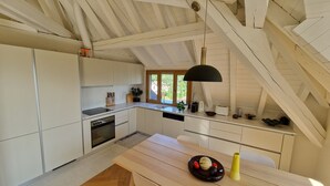 Une cuisine moderne avec des meubles blancs, un four encastré, un évier et un coin repas doté d’une table en bois.