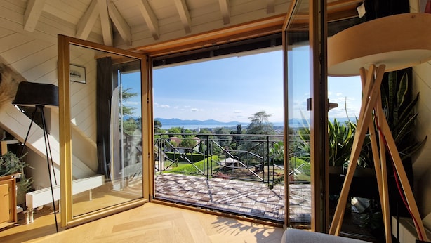 Une pièce dotée d’une grande porte-fenêtre coulissante donnant sur un balcon avec vue sur les montagnes et un lac.