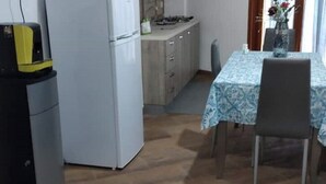 Cuina compacta amb nevera, fogó i armaris. Hi ha una taula de menjador amb caires i un vas amb flors a sobre.