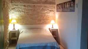 Un dormitorio con pared de piedra, una cama con cubrecama azul, dos lámparas de noche y un equipo de aire acondicionado instalado en la pared.
