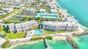 Eine Vogelperspektive eines Küstenresorts mit mehreren Gebäuden, einem Schwimmbad und einem Steg, der ins Wasser führt.