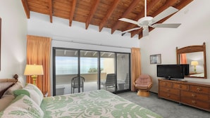 Ein Schlafzimmer mit einem großen Bett, einem Deckenventilator, einem Fernseher, einem Schminktisch und einer Glasschiebetür, die auf einen Balkon führt.