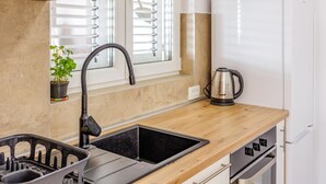 Una cocina con un lavamanos negro, una tetera y una ventana con persianas.