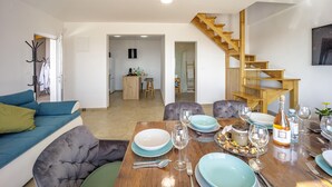 Una sala moderna con comedor, una escalera y una cocina al fondo.