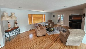 A spacious living room with hardwood flooring, a brown sofa, a coffee table, and a television. - Spacious 1 story Home in Rapid City Historic District (Rapid City)