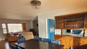 A modern living room with a wooden dining table and blue upholstered chairs, a kitchen with wooden cabinets, and a chandelier. - Spacious 1 story Home in Rapid City Historic District (Rapid City)