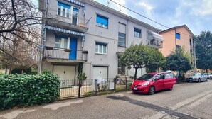 Eine Wohnstraße mit mehrstöckigen Gebäuden, ein rotes Auto, das am Straßenrand geparkt ist, und einem klaren Himmel.