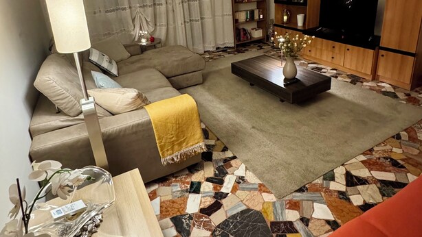 Ein modernes Wohnzimmer mit einem Ecksofa, einem Couchtisch, einem Fernseher und einem Bücherregal.
