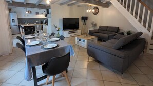 A modern living room with a grey sofa, dining table set for six, and exposed wooden beams on the ceiling. - Maison Charentaise (Juillac-le-Coq)