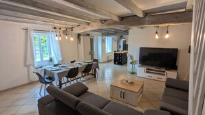 A modern living room with a sofa, TV, and dining area with chairs and a table. - Maison Charentaise (Juillac-le-Coq)