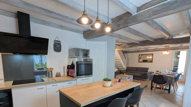 A modern kitchen with a central island, built-in oven, and microwave. There is a dining area with a table and chairs. - Maison Charentaise (Juillac-le-Coq)