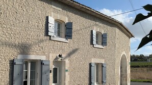 A stone building with a door and windows, a small porch, and a sign indicating a number. - Maison Charentaise (Juillac-le-Coq)