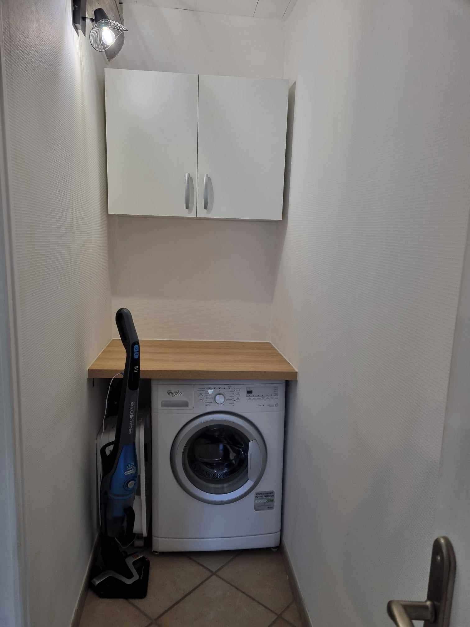 A laundry room with a washing machine, a cabinet above it, and a vacuum cleaner to the left.