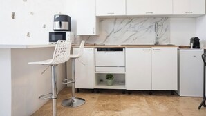 A modern kitchen with white cabinetry, a marble backsplash, a coffee machine, and a bar stool. - Appartement Proche de Disney (Chalifert)