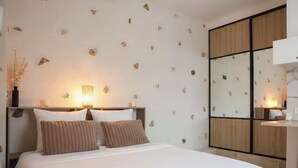 A neatly made bed with a white duvet and two brown pillows, a bedside table with a lamp, and a wall with a geometric pattern. - Appartement Proche de Disney (Chalifert)