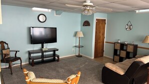 Een woonkamer met een flatscreen televisie, een plafondventilator, een houten stoel, een bank, een lamp en een deur.