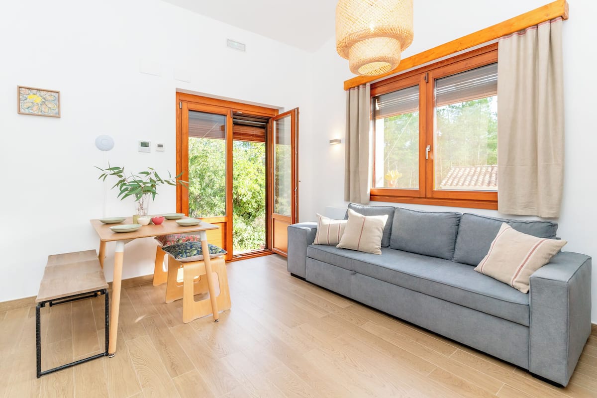A living room with a grey sofa, wooden dining table, and a large window with curtains.