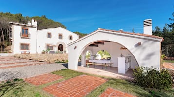 Una villa blanca con un camino de piedra, un área de comedor al aire libre cubierta y vistas del paisaje circundante.
