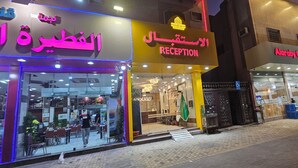 Une réception d’hôtel avec une enseigne en arabe et en anglais, une entrée bien visible et un restaurant situé à proximité.