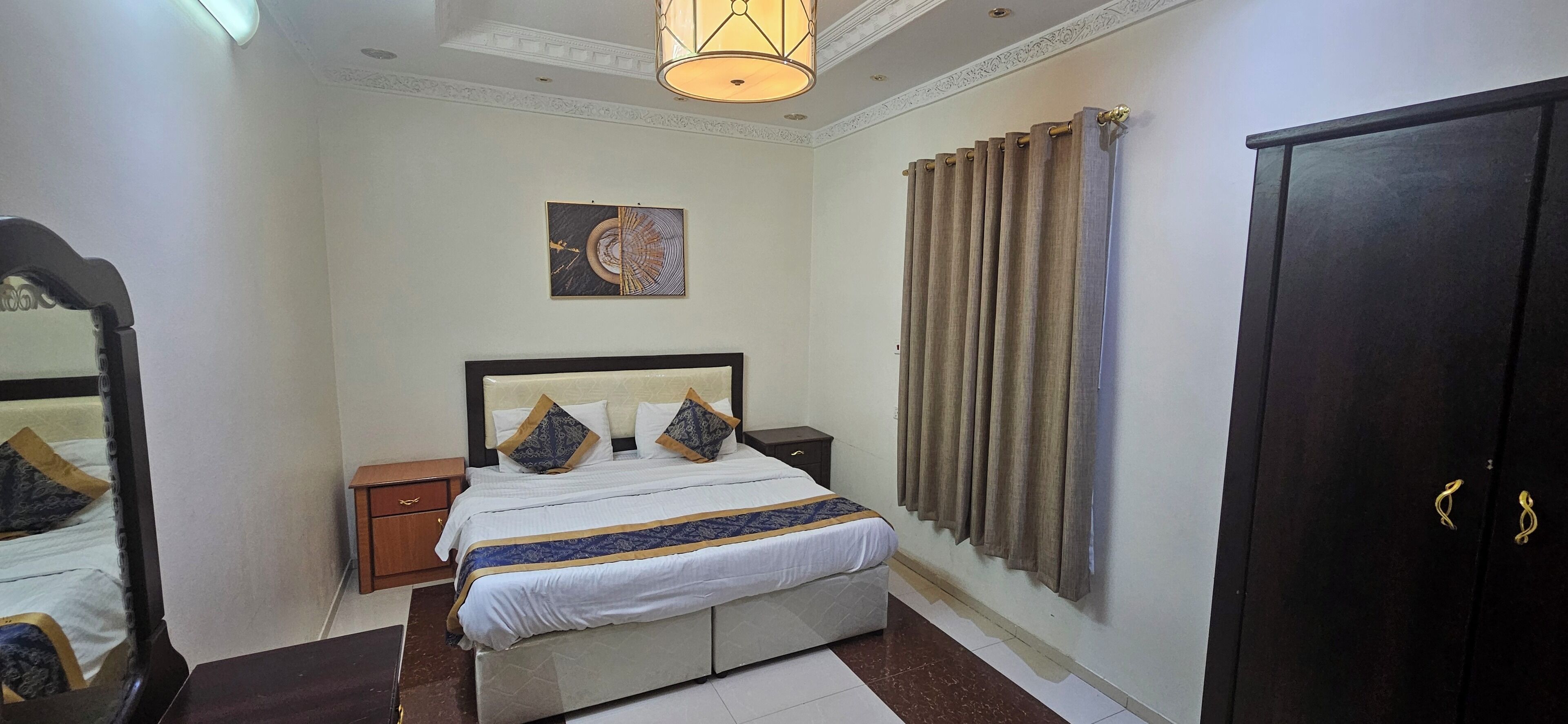 A hotel room with a bed, nightstand, wardrobe, and a ceiling light fixture.