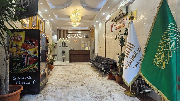 Un hall d’hôtel équipé d’un distributeur automatique, d’un espace salon et d’un drapeau vert orné d’inscriptions en caractères arabes.