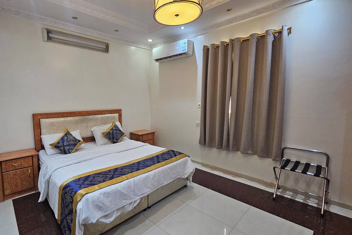 A neatly arranged bedroom with a bed, bedside tables, a nightstand, a chair, and a window with curtains.