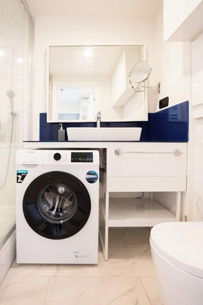 A compact bathroom with a washing machine, a sink, and a toilet.