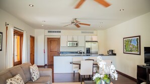 A modern living room with a sofa, a dining area, a kitchen with a central island, and a ceiling fan.